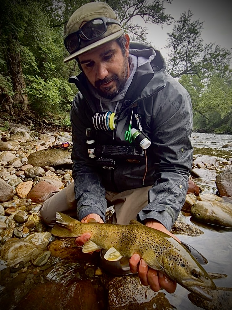 Benoît Moreno, guide de pêche à la mouche, présentant une truite fario au bord d'une rivière de montagne.